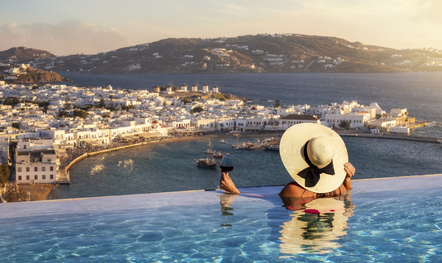 Abeona Luxury Solo Female Traveler Enjoying Wine in an Infinity Pool Overlooking a Mediterranean Town