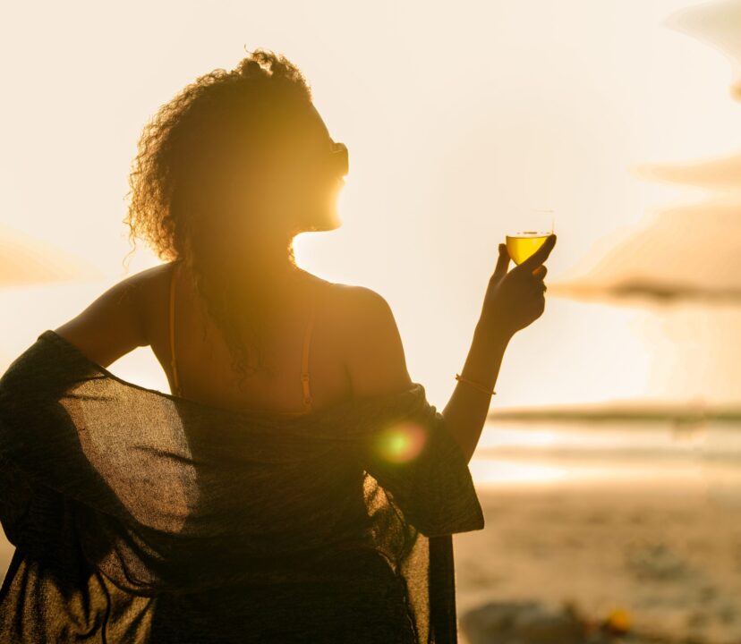 Woman enjoys a luxury solo female travel moment - looking wistfully at the sunset whilst enjoying a fabulous drink