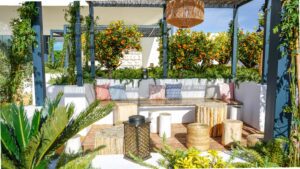 A seating area in the gardens of the luxury hotel with tables and pillows for comfort, surrounded by greenery and orange trees.