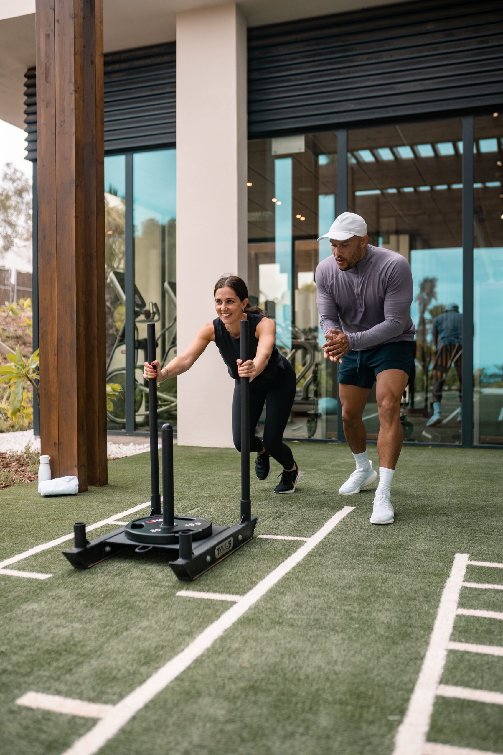 A woman pushing a sled whilst being trained by a coach in the hotels luxury gym facilities.