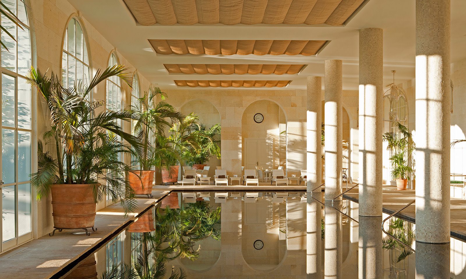 The indoor pool at the luxury hotel spa with loungers along the edge of the pool, potted plants and large windows letting in natural light.