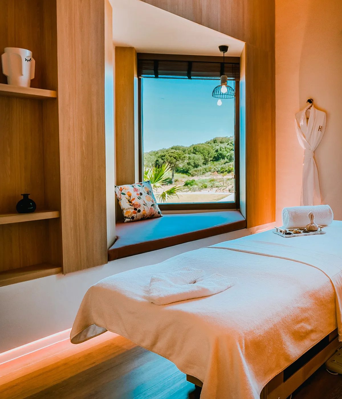 A room at the luxury SO/Sotogrande spa with a massage table, a robe and a window seat with views of the Andalucian landscape.