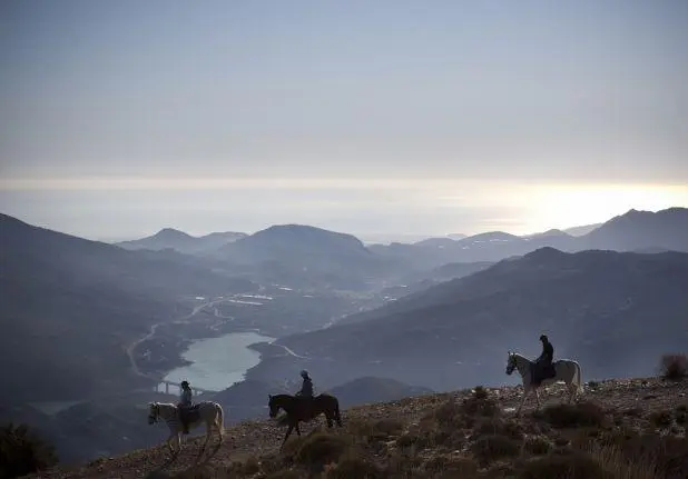 3 horseriders trekking in the mountains and hills above Granada with a hazy vieiw of a reservoir and the sea in the distance