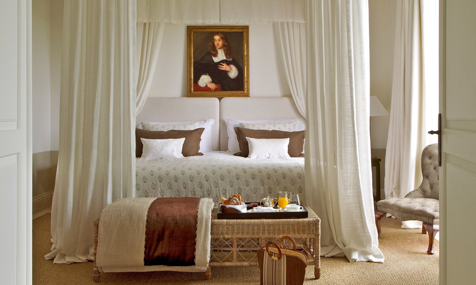 A bedroom in the luxury hotel showing a four poster bed, an armchair and a tray at the end of the bed with a variety of breakfast items.