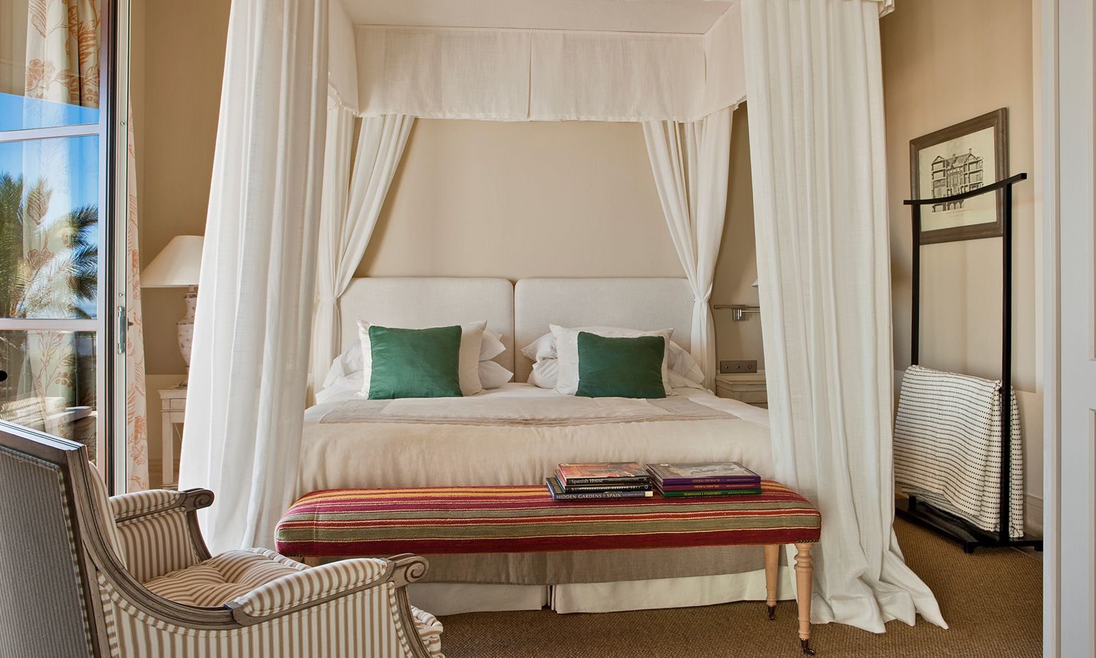 A bedroom in the luxury hotel with a large four poster bed, an armchair and a door opening up onto the balcony.