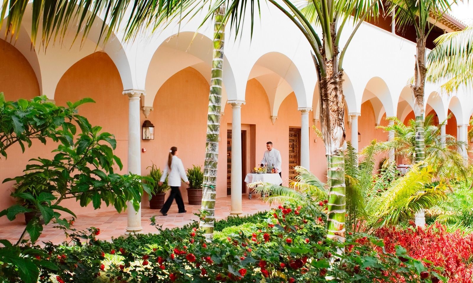 A view of the hotel surrounded by vibrant greenery with two workers at the hotel.