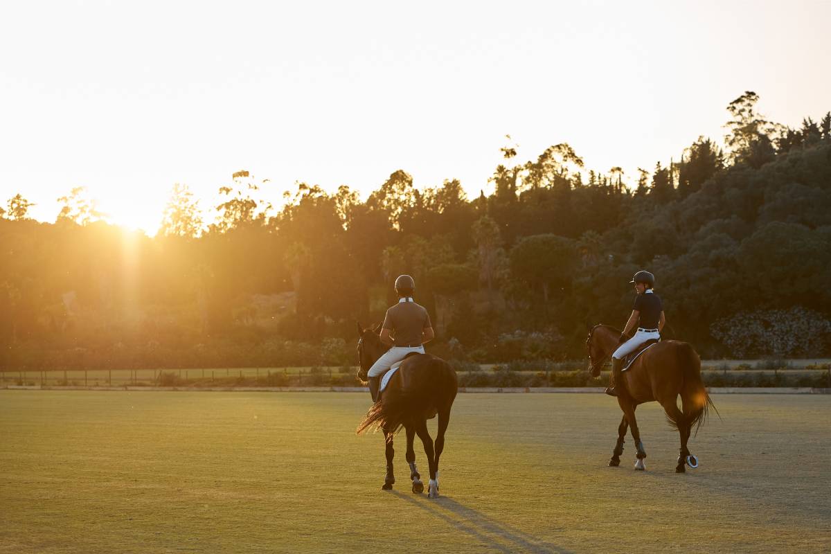 Two riders on horses walking across the polo grounds at Santa Maria Equestrian Club in Sotogrande Spain with the sun setting in the background