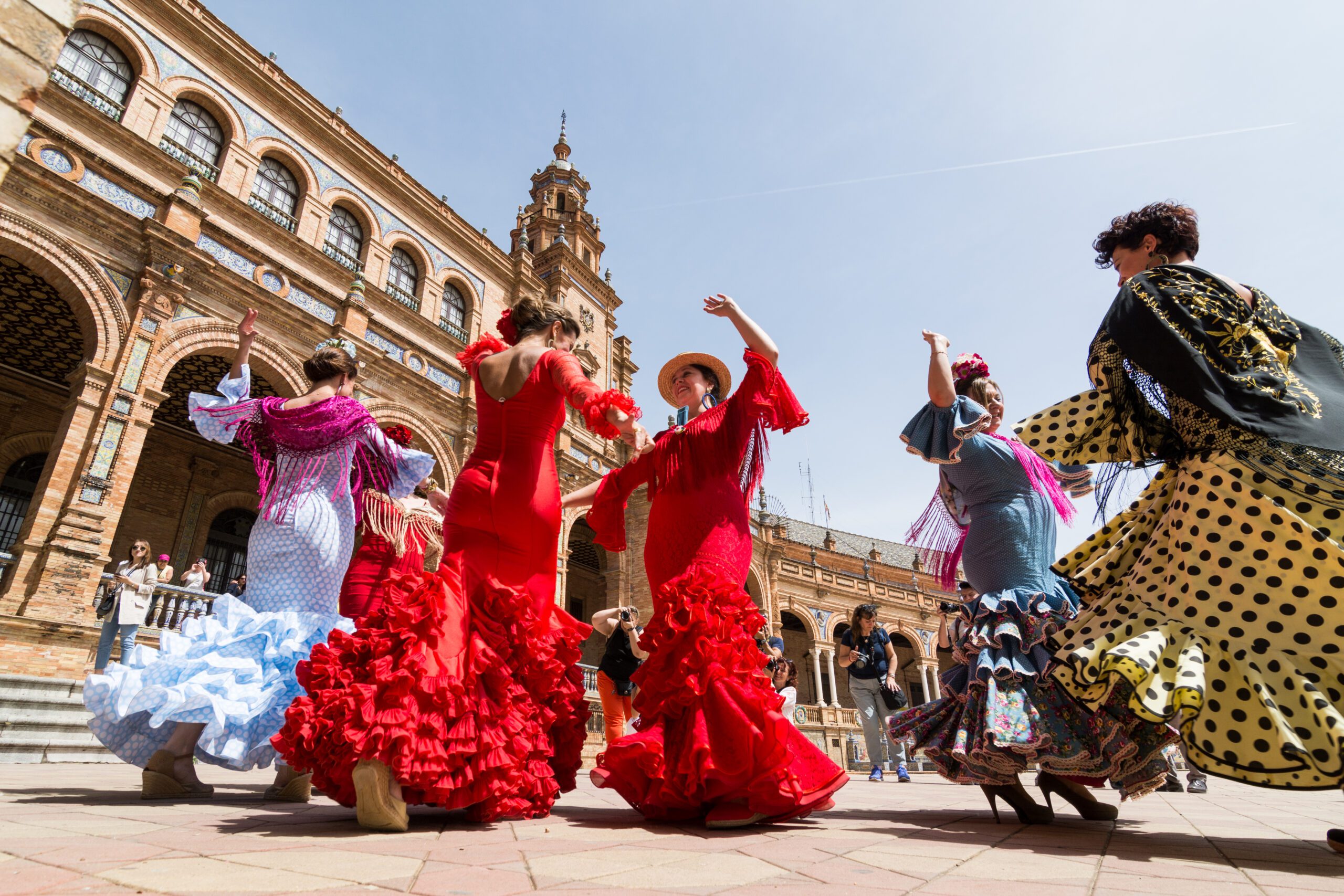 Women dancing flamenco in traditional flamenco dresses in red in the Plaza de España during the famous Feria festival