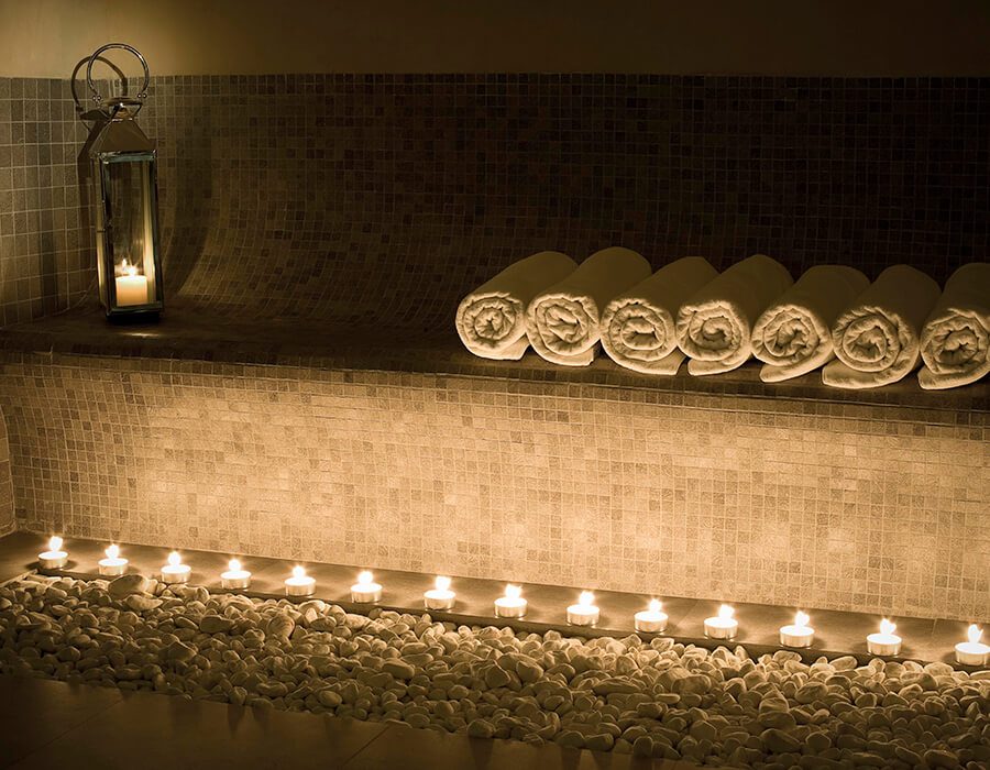 A candle lit room in the luxury spa with neatly rolled towels for the guests.