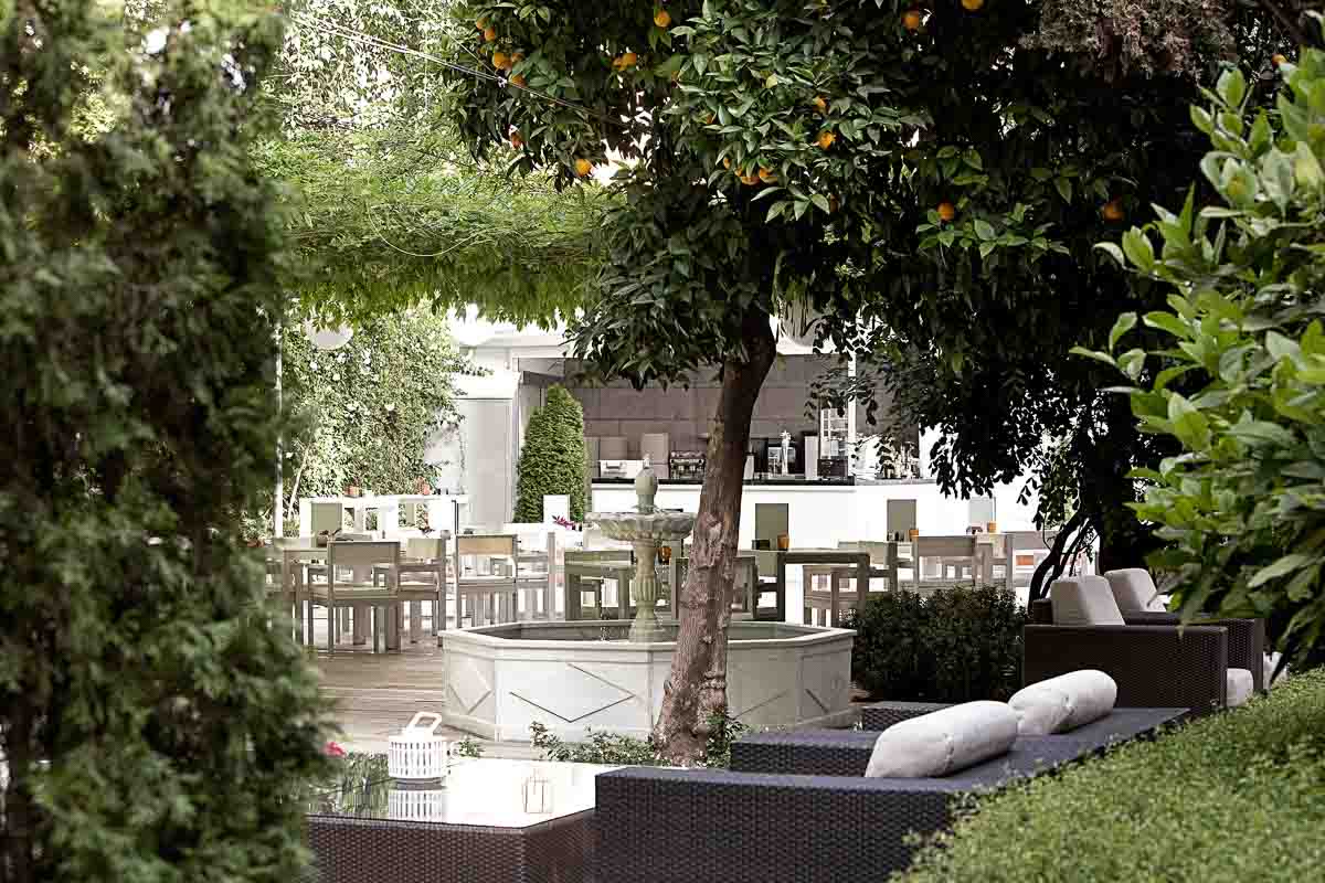 An outdoor seating area surrounded by greenery and a water fountain.