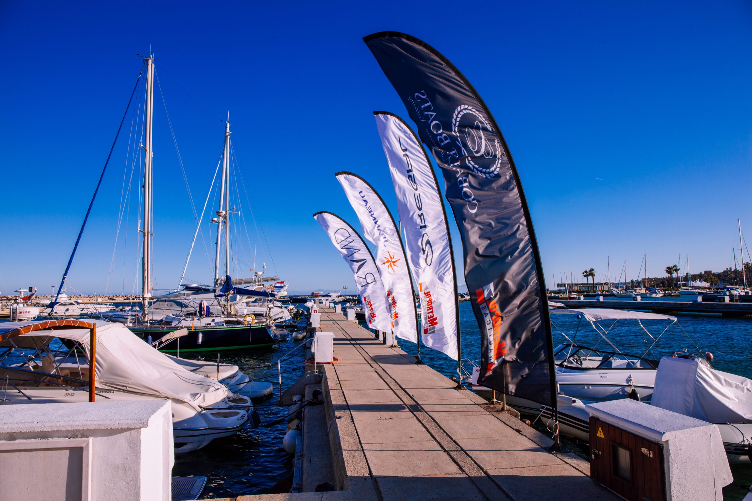 Large black and white flags or sails blowing in the wind attached to the pier in Puerto Sotogrande with yachts in the background under a deep blue sky