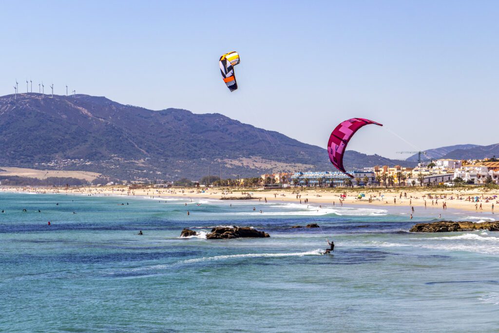 2 colourful Kites in the blue sky above the kitesurfers on the flat blue sea at Playa de los Lances, Los Lances Beach, Province of Cadiz, Andalucia, Spain