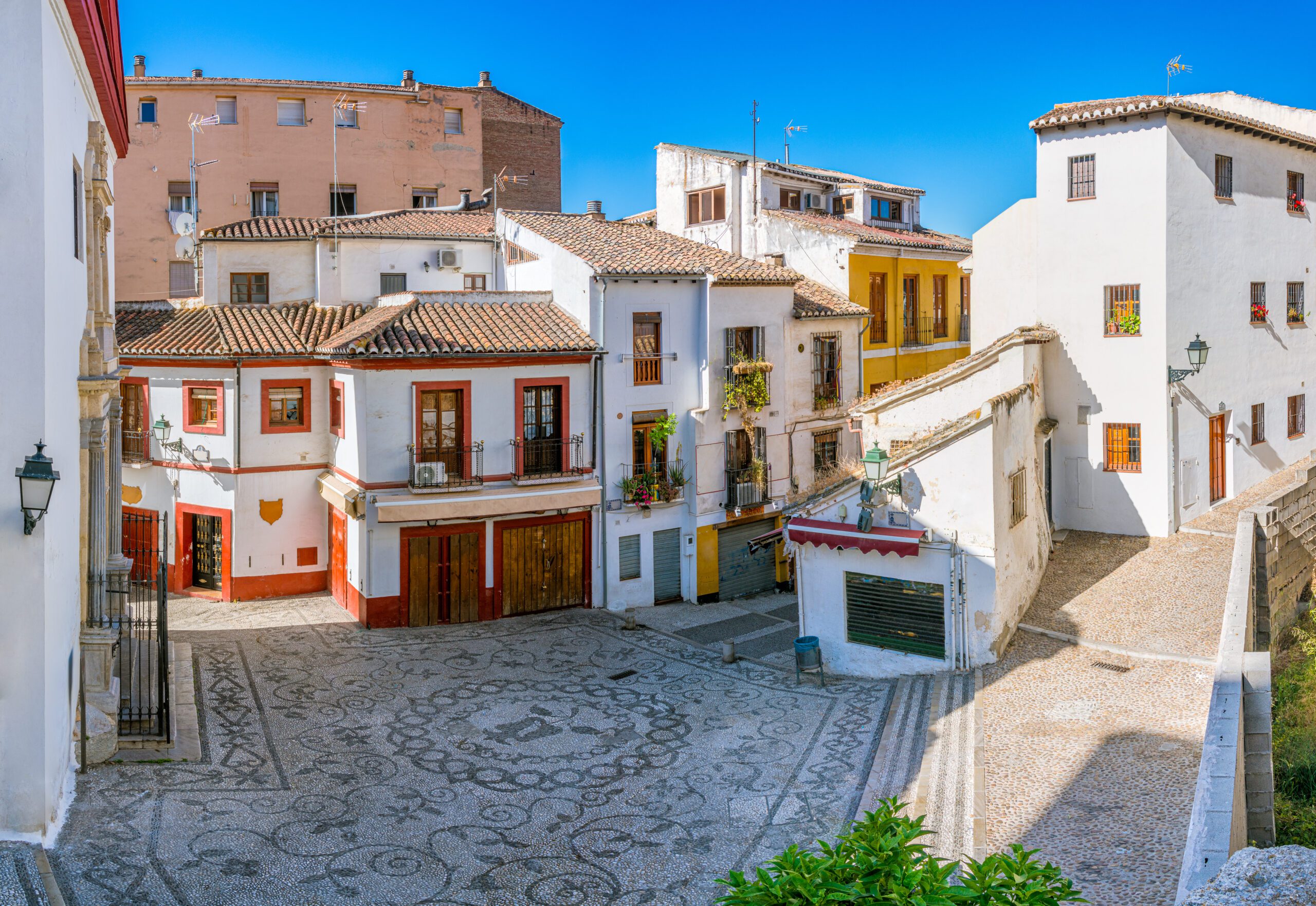 A street in the Albacin Quarter in Granada on a sunny afternoon with a bright blue sky.