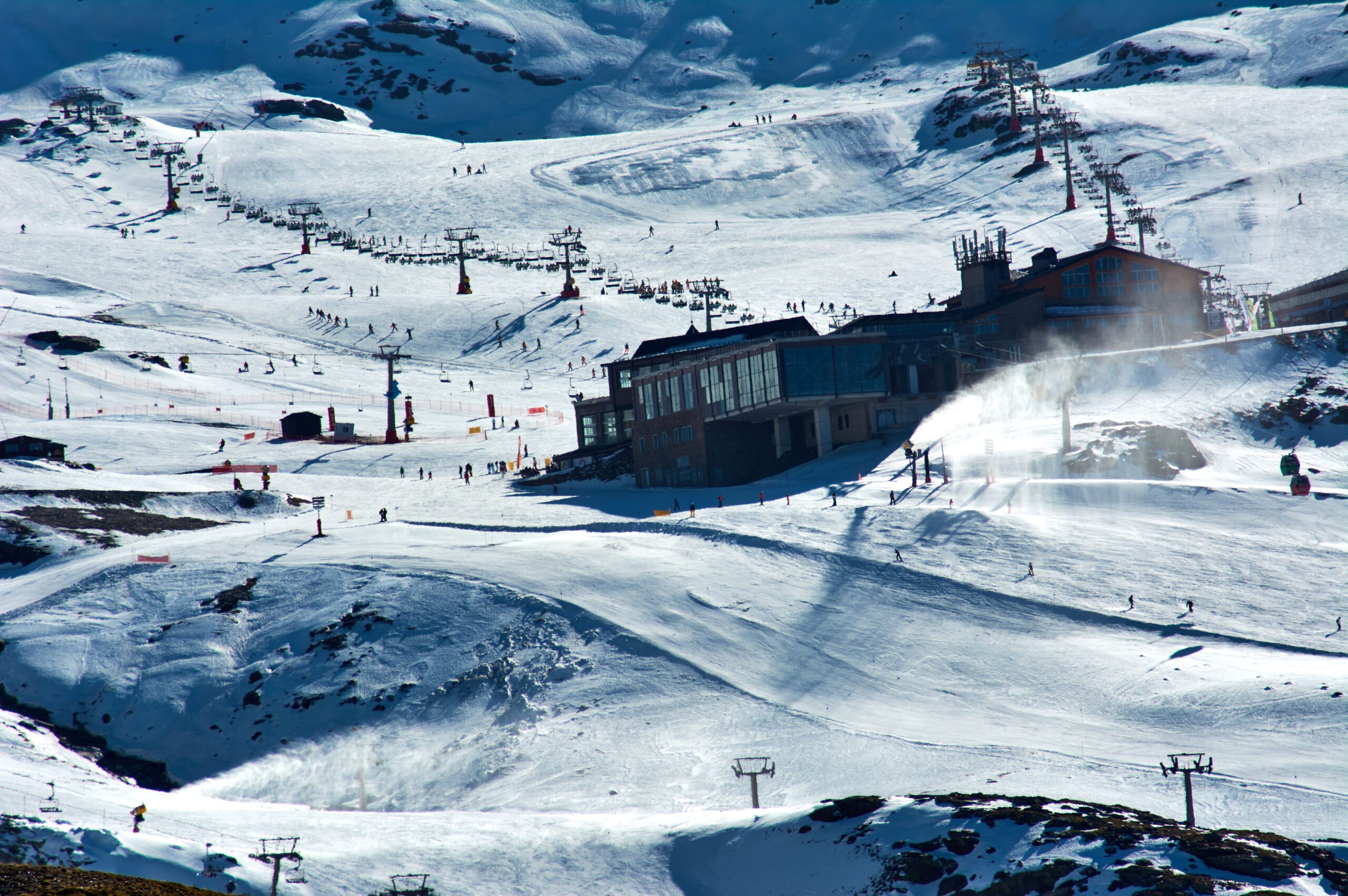 View of the Ski Resort of Sierra Nevada in Granada Spain, with undulating snowy hills and ski chalets or facilities and ski lifts. In the low Snow season. Using artificial Snow cannons