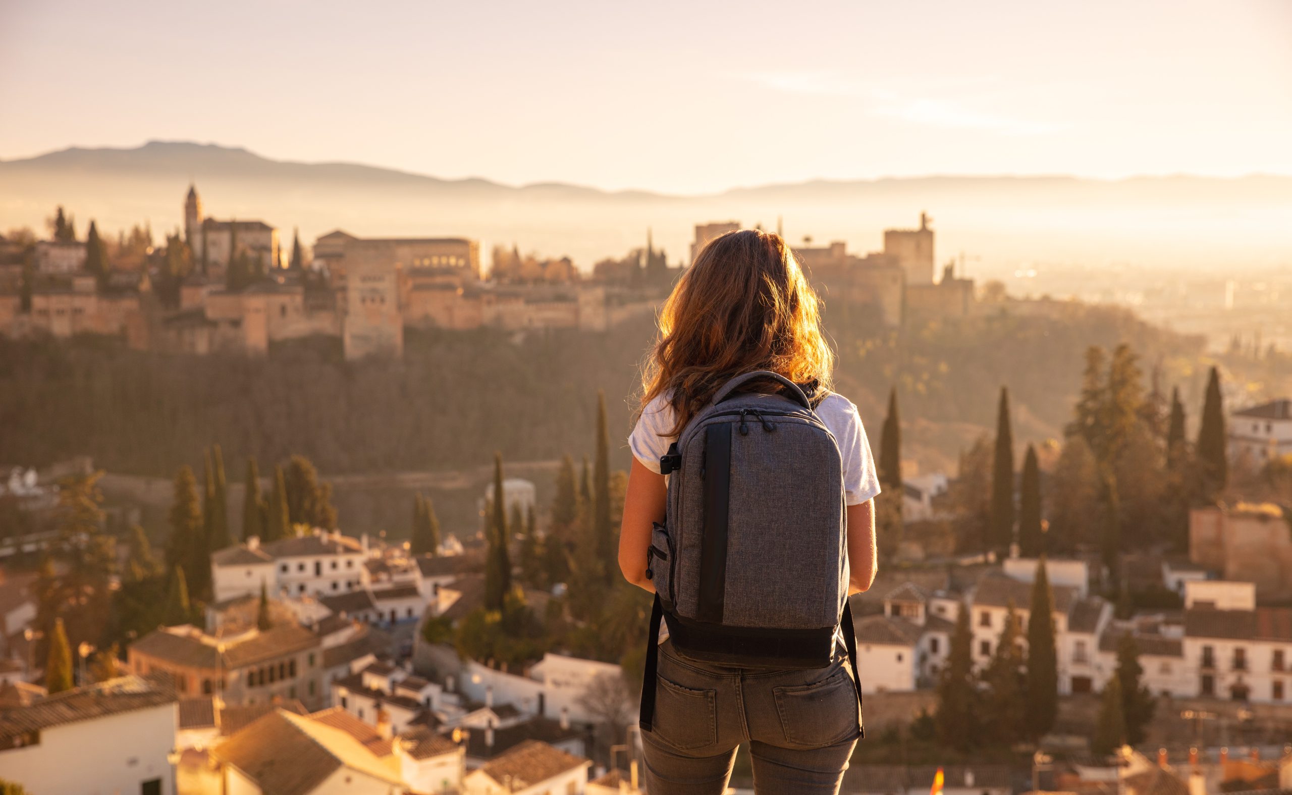 A woman standing in Granada looking over at Alhambra Palace and the mountains in the distance.