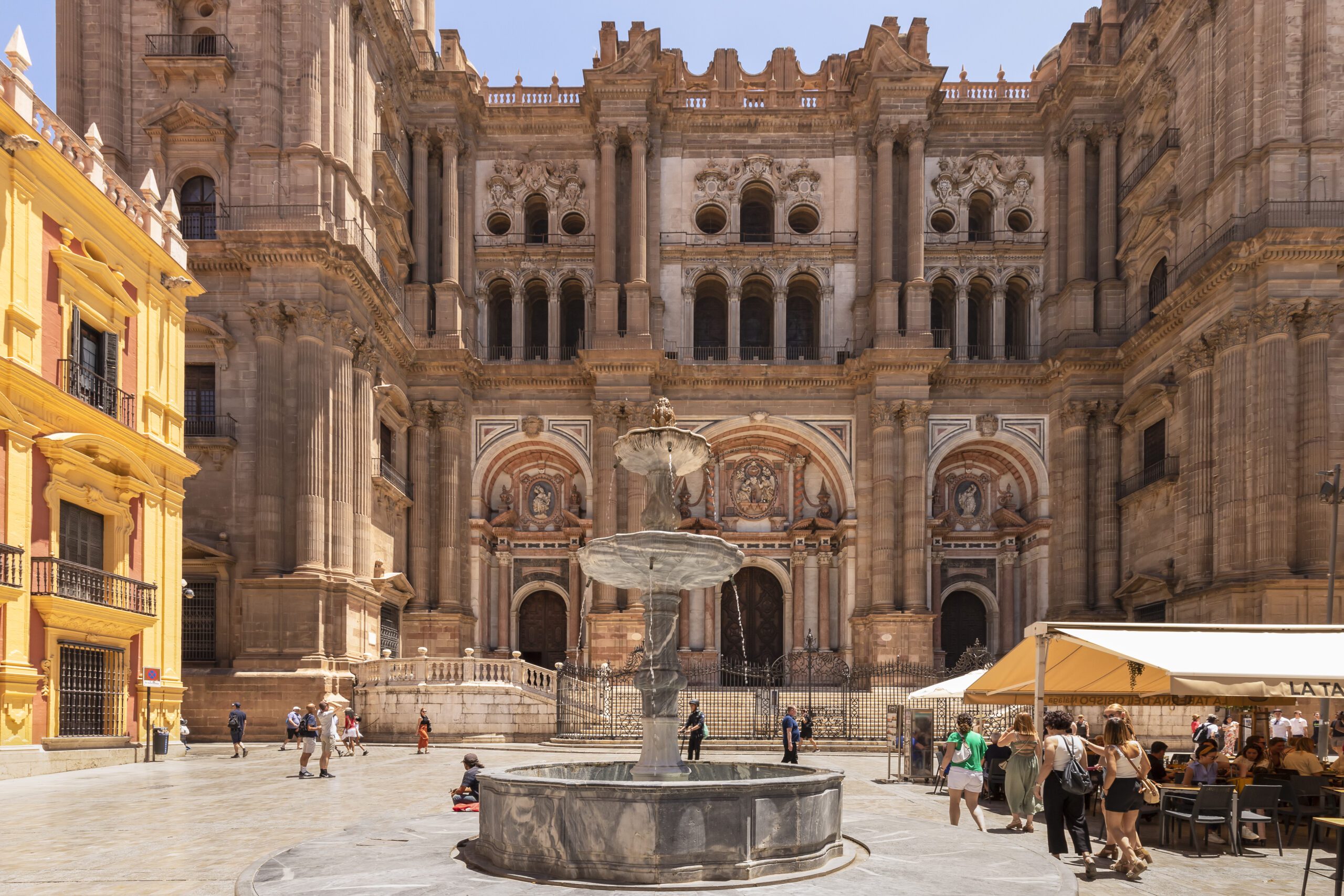 A view of the Cathedral of malaga with a fountain and tourists in the town square in the foreground