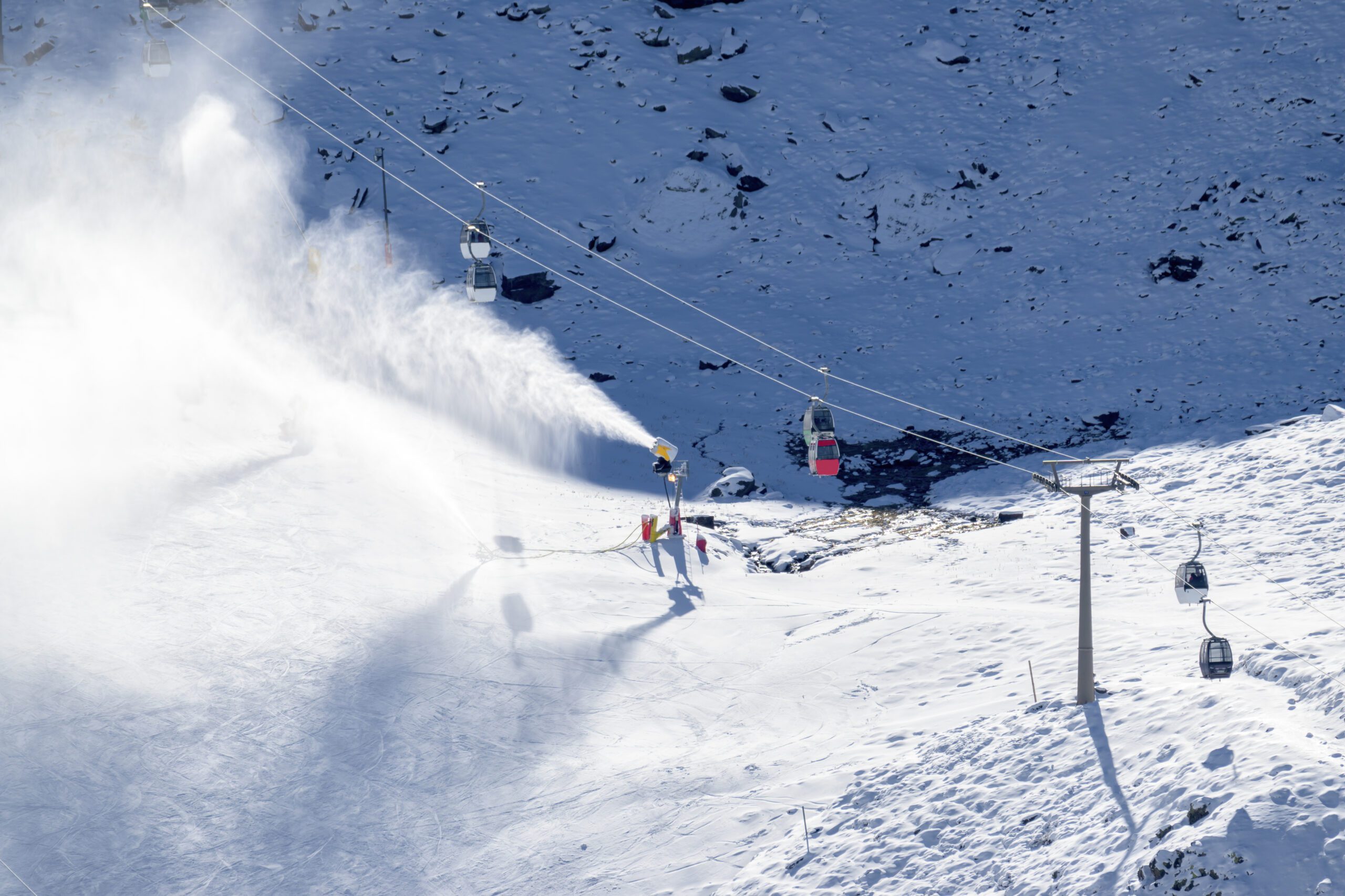 Snow cannons spreading artificial snow in the Sierra Nevada in Granada Spain. Ski cable cars in view with mountain in background.