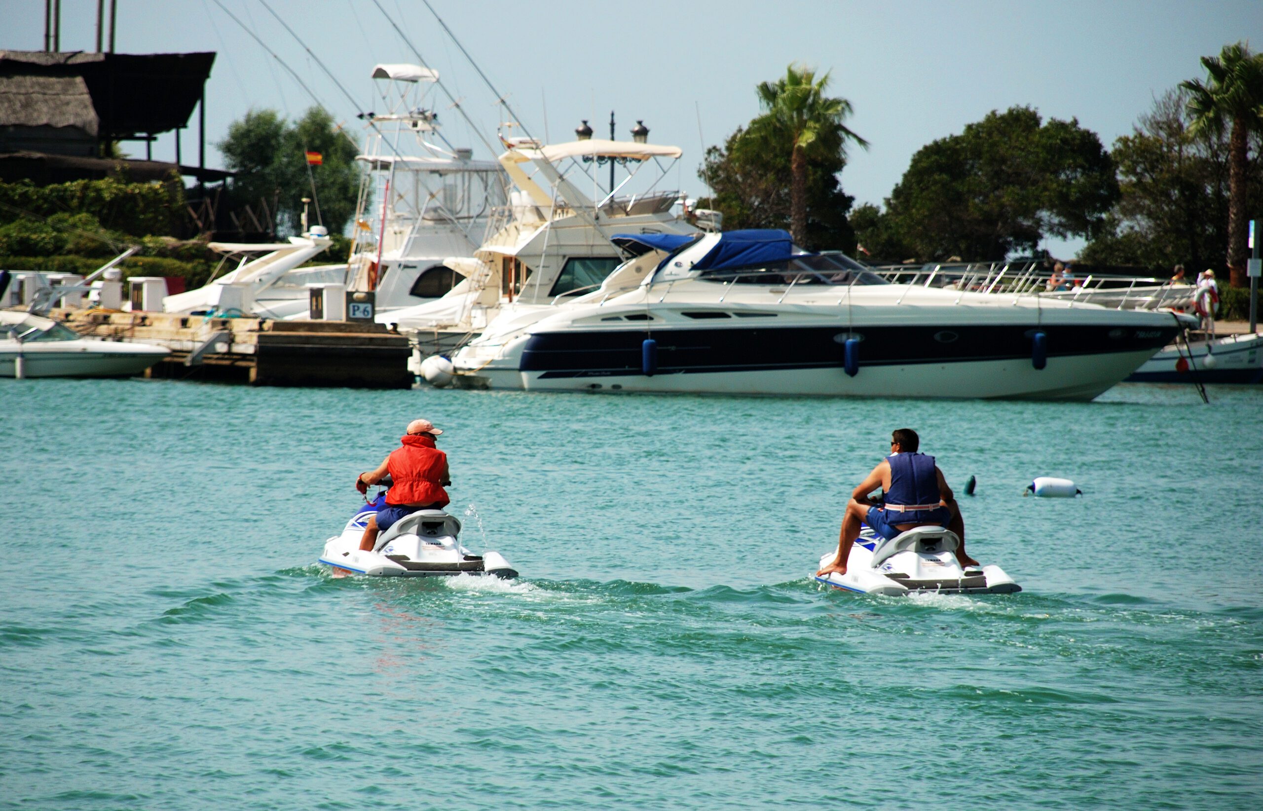 Two Jetskis arriving into Puerto Sotogrande on calm waters with a luxury yacht in the background