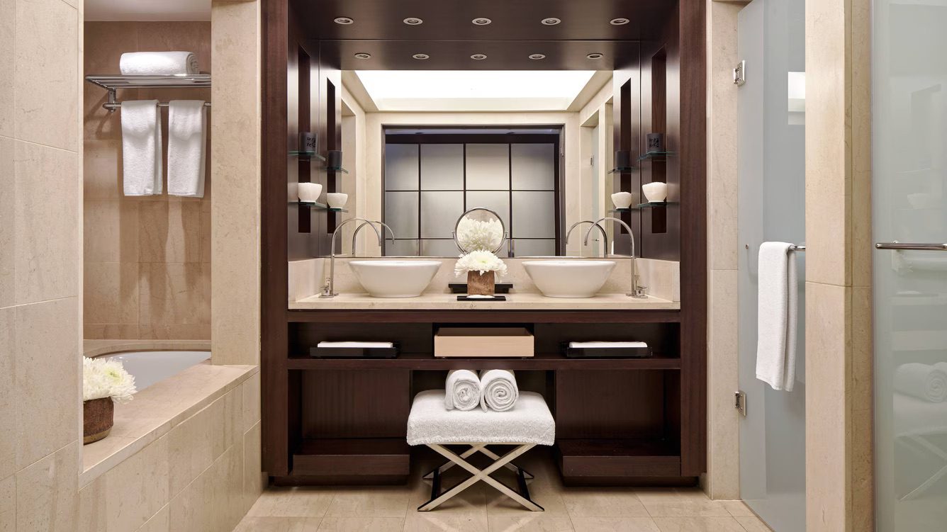 A luxury bathroom with a large mirror above a double sink, a bathtub to the left and a shower to the right.