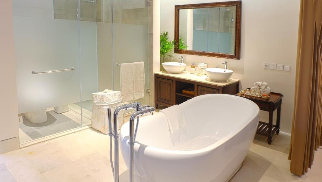 A luxury bathroom with a bath in the centre, wooden sideboards with two sinks and a mirror hung above them, complete with a frosted glass screen covering the toilet and shower facilities.