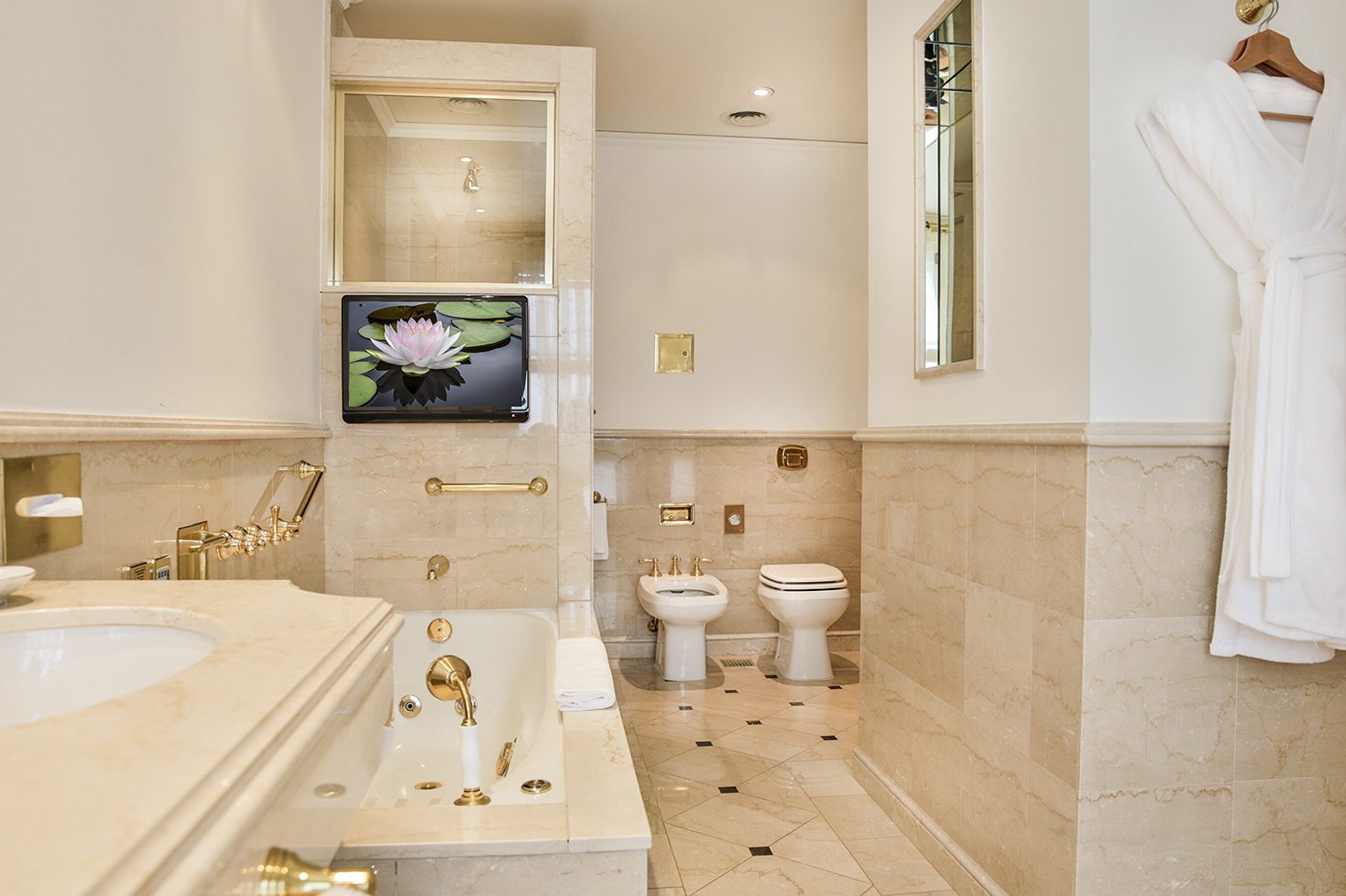 A luxury bathroom with a grand bath, shower, sink and toilet with brass finishes, complimenting the marble tiles.