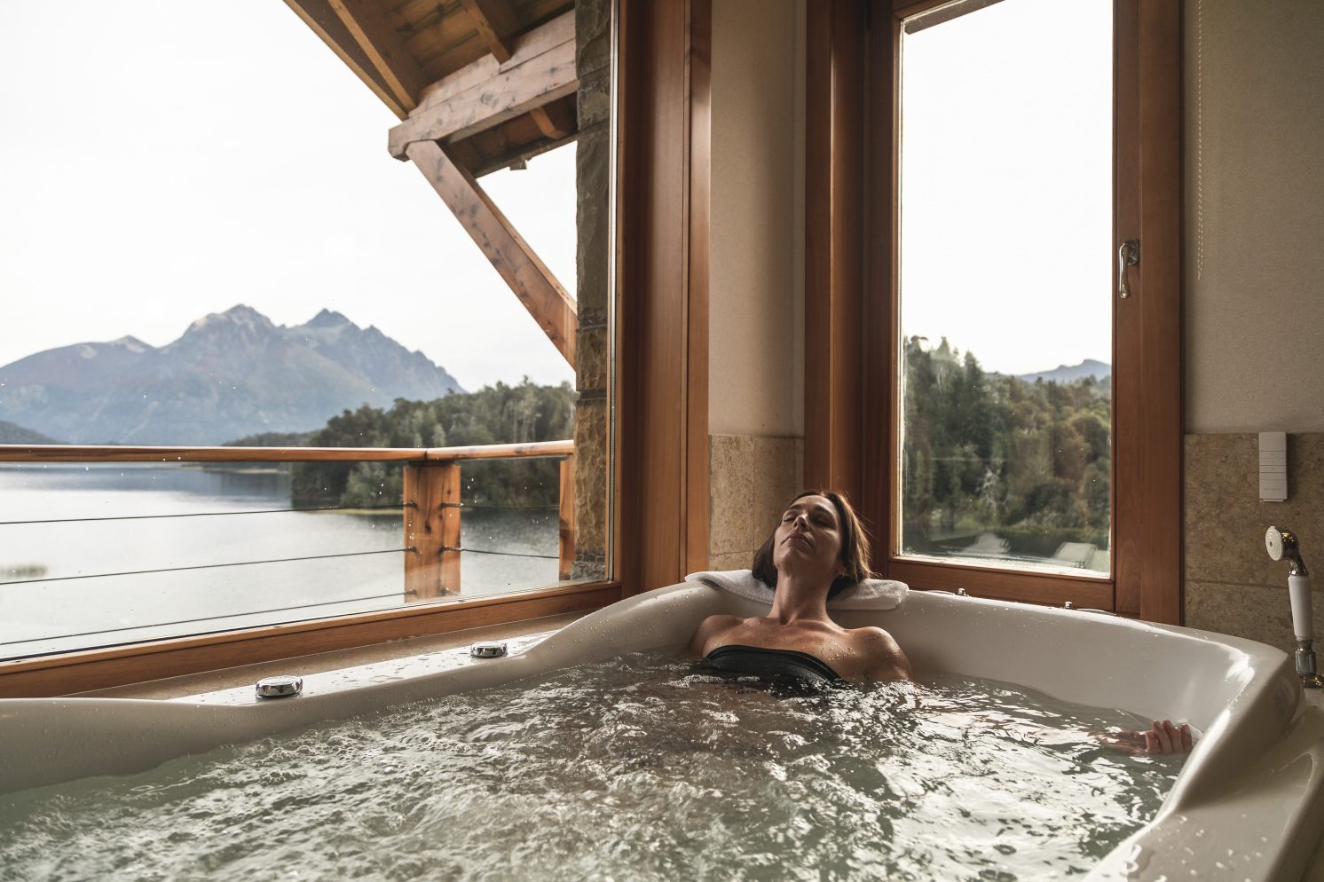 A woman relaxing in a luxury bathtub with incredible views of the mountains and lake.