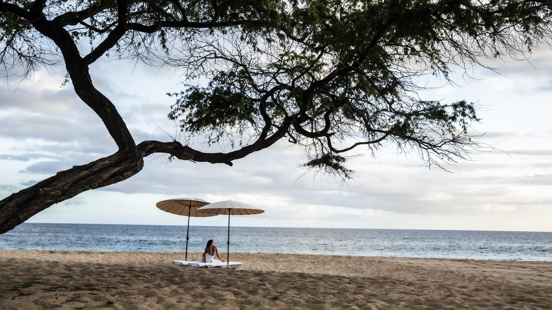 A woman lounging under a sun umbrella on the pristine Hulopoe beach, enjoying the serene ocean view.