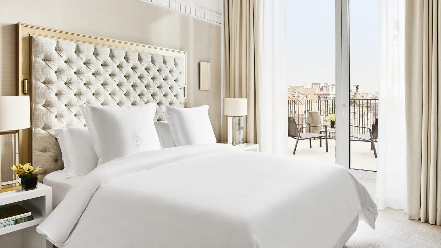 A bedroom at the luxury hotel, featuring a large bed with pristine white bedsheets, complete with glass doors leading onto the private terrace with views over Madrid.