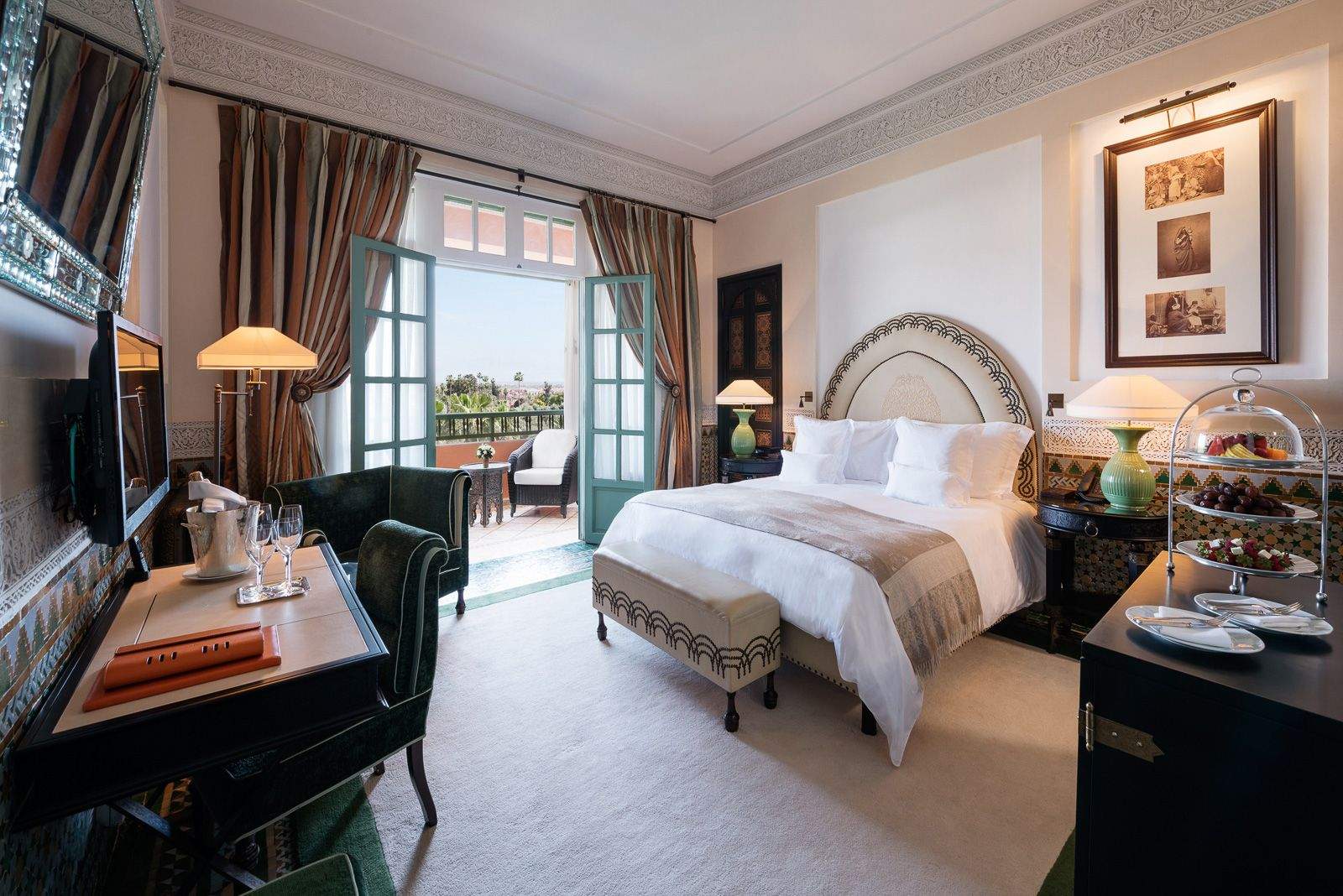 Elegant bedroom featuring a spacious bed with pristine white bedsheets, traditional moroccan furnishings and a balcony with a stunning view of Marrakech.