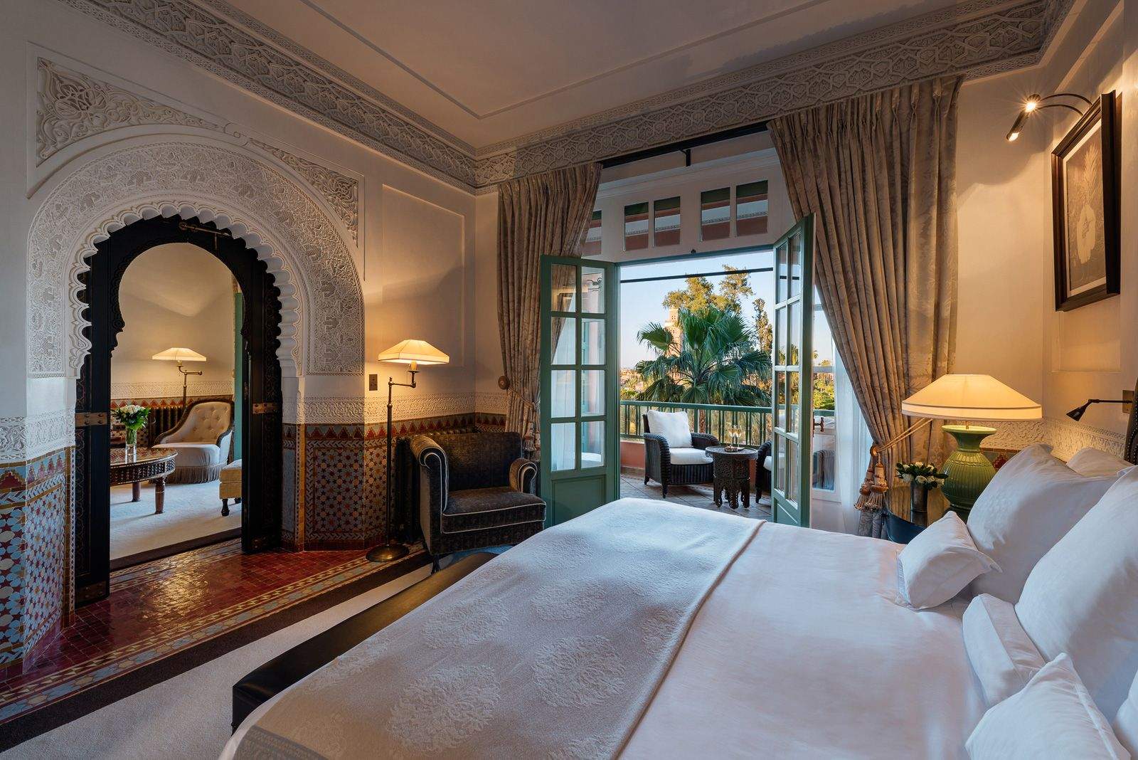 Elegant bedroom featuring a spacious bed with pristine white bedsheets, traditional moroccan furnishings and a balcony with a stunning view of Marrakech.