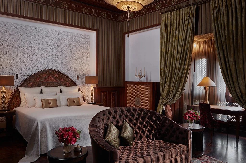 Luxurious Moroccan-inspired bedroom with pristine white bedsheets, an elegant chair and a desk with a picturesque window view.