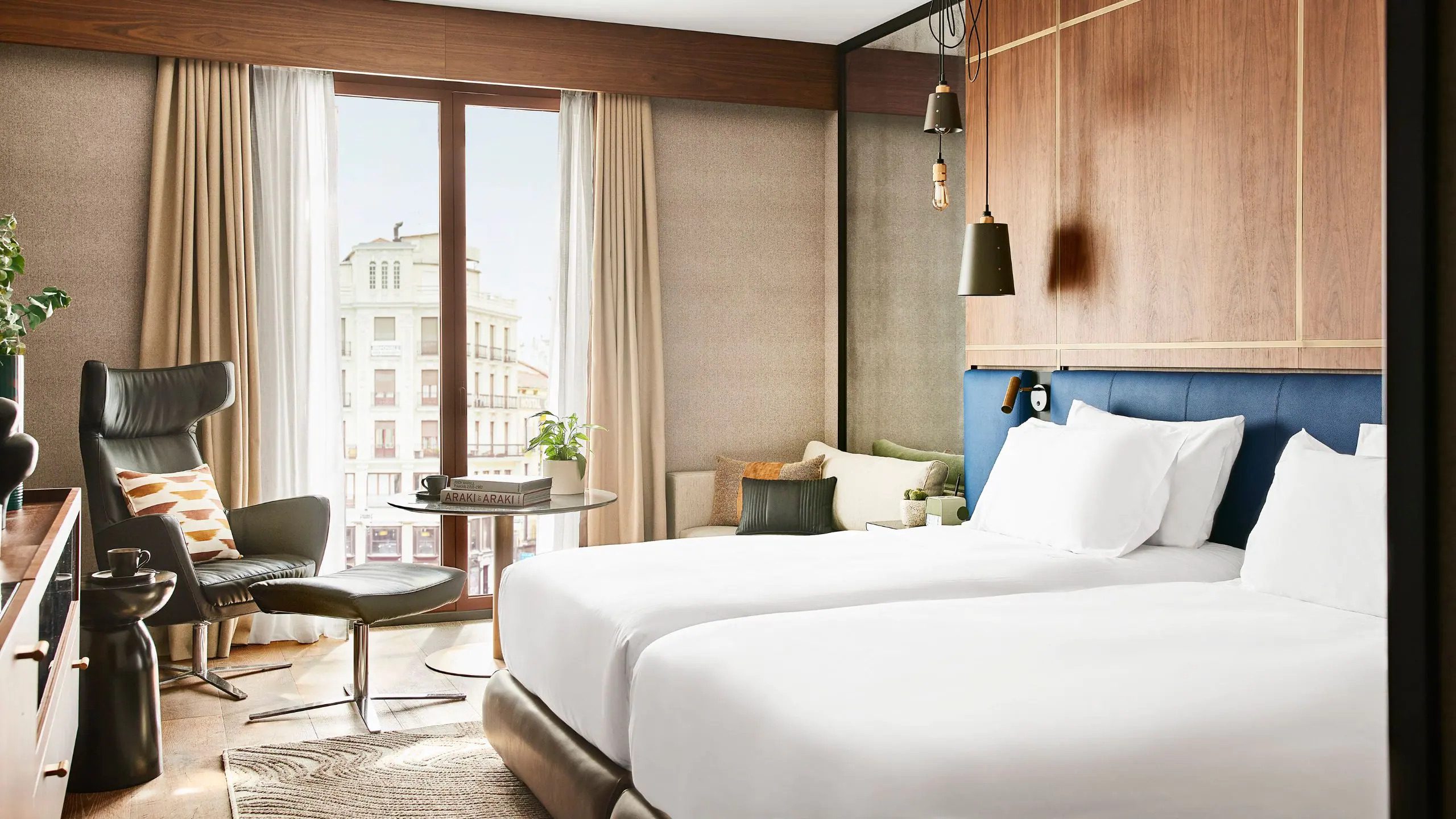 Bedroom with Twin Beds at the Thompson Hotel in Madrid with a floor to ceiling window showing the Madrid buildings outside.