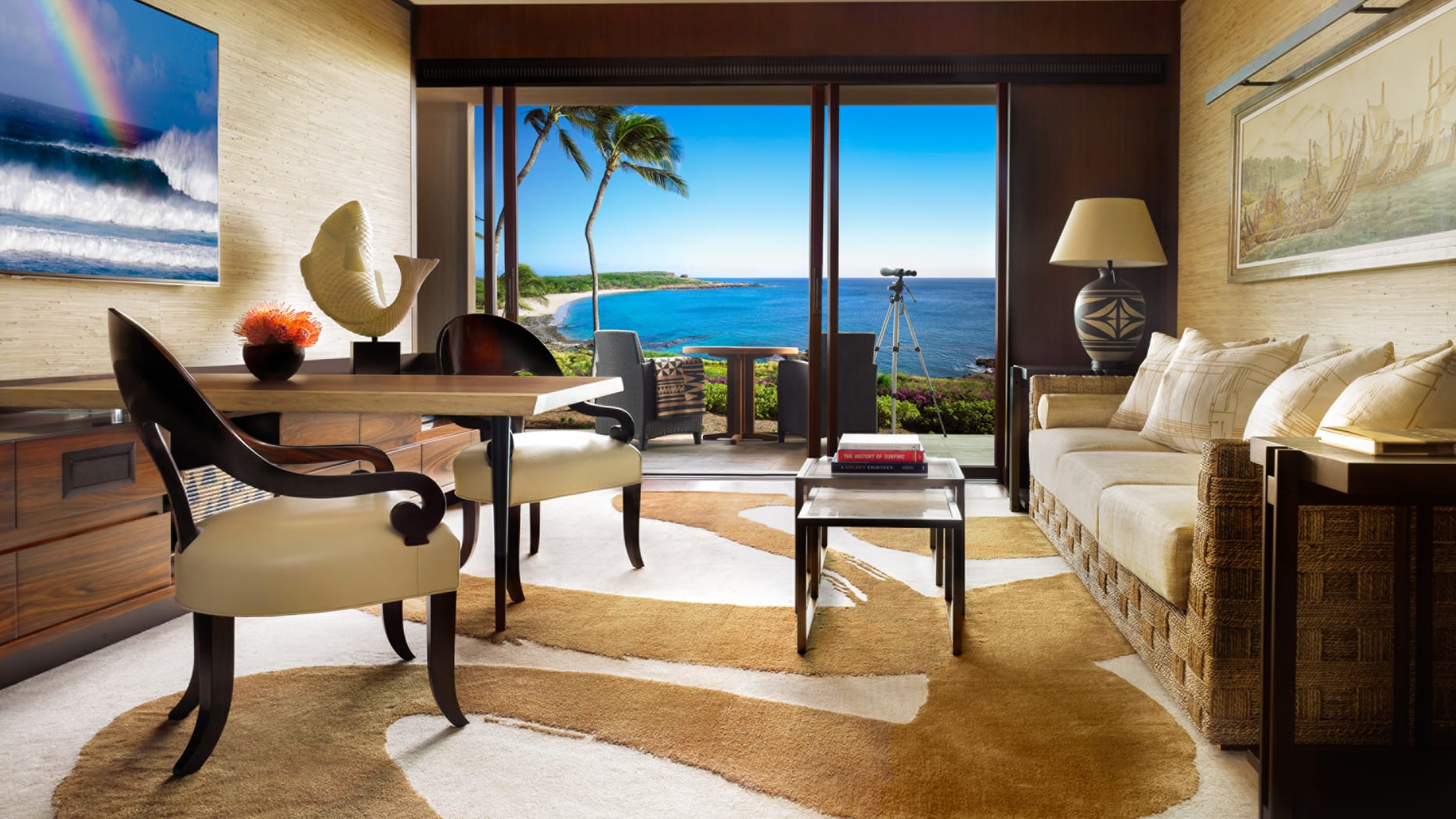 A living area with sofas and chairs to relax, floor-to-ceiling glass opening up onto a balcony, overlooking Hulopoe Bay.