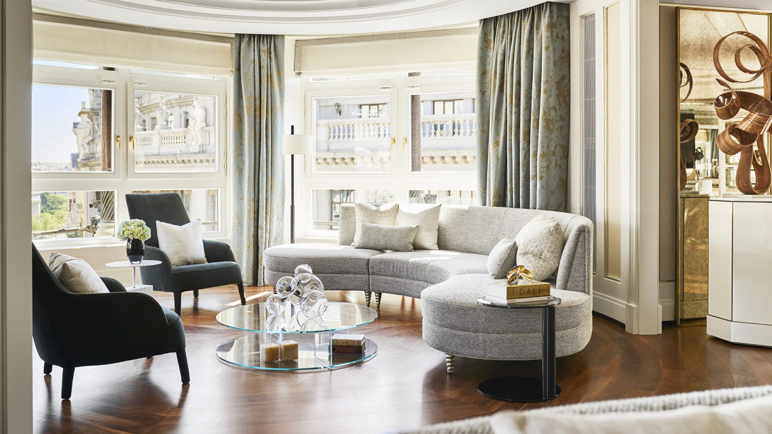 A living area in the luxury hotel, featuring two armchairs, a sofa and large windows showcasing the views of Madrid.