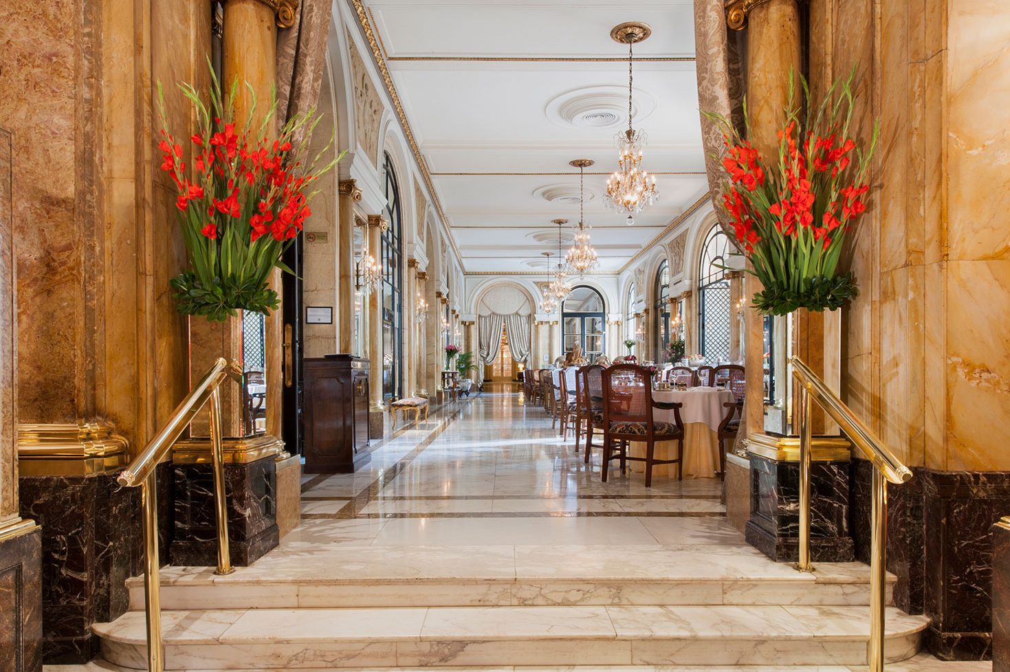 A grand entrance to a dining area at the luxury hotel with marble floors and walls, potted plants and chandeliers lining the ceiling.