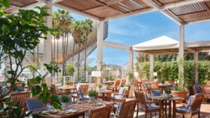 A spacious outdoor dining area at the luxury hotel, with canopies covering the tables and chairs, greenery and views of Barcelona.