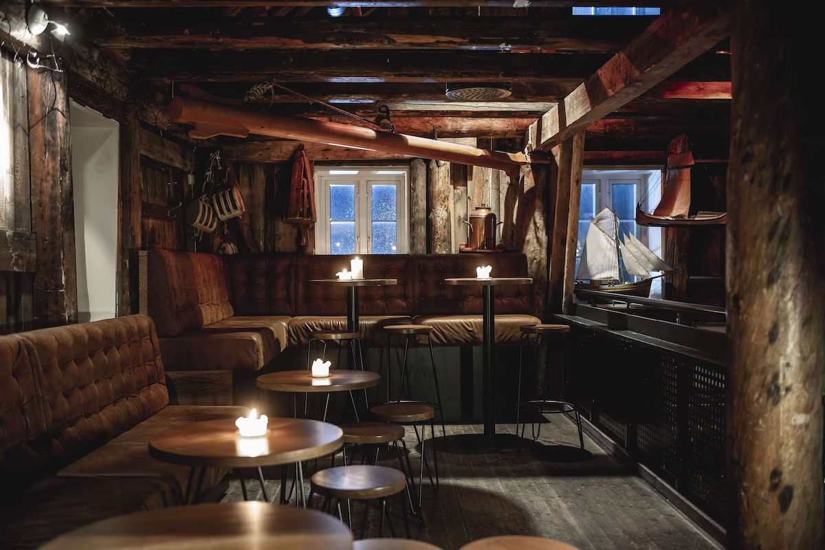 A dark dining area with wooden walls and beams across the ceiling, candles lit on the tables and leather seating.