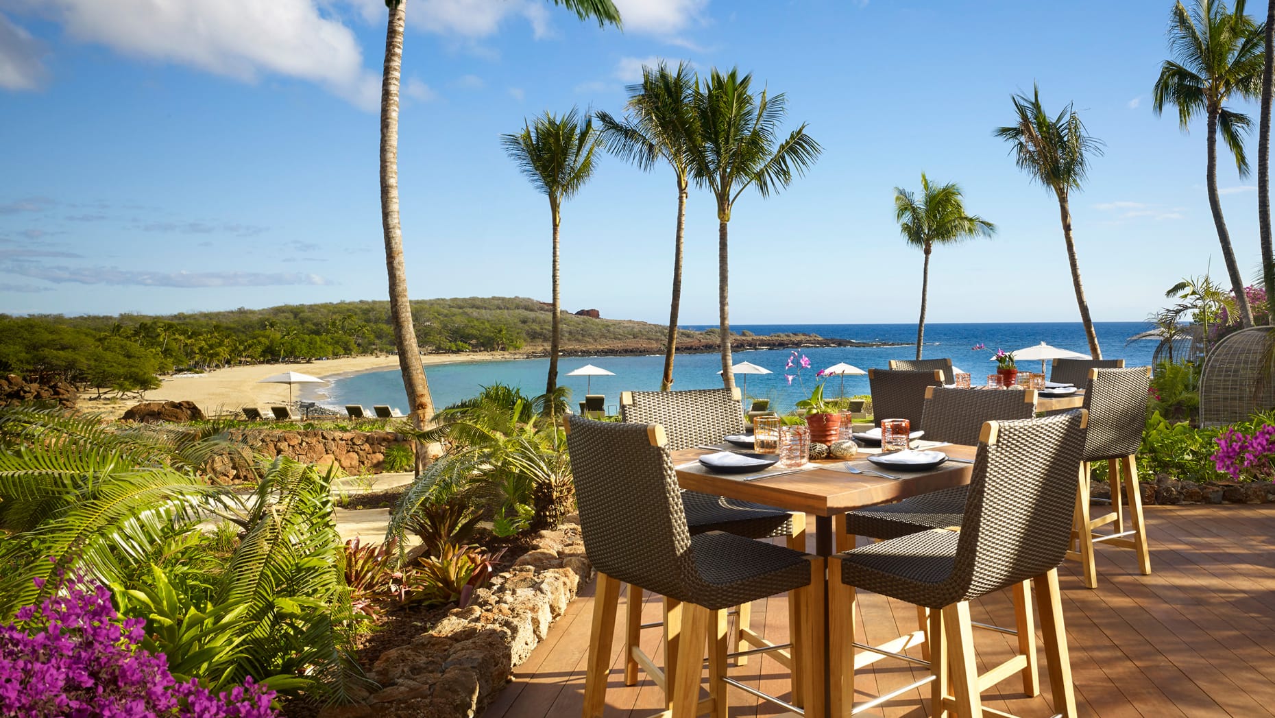 Elegant oceanfront dining area featuring a table, chairs, and umbrellas, creating a serene and picturesque setting.