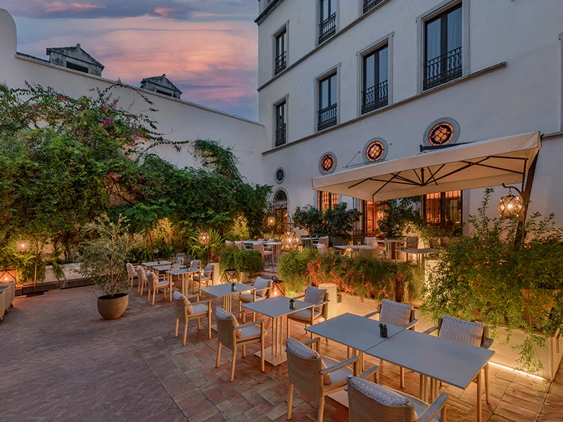 A dining area outside the luxury hotel with an array of tables and chairs surrounded by lush plants.