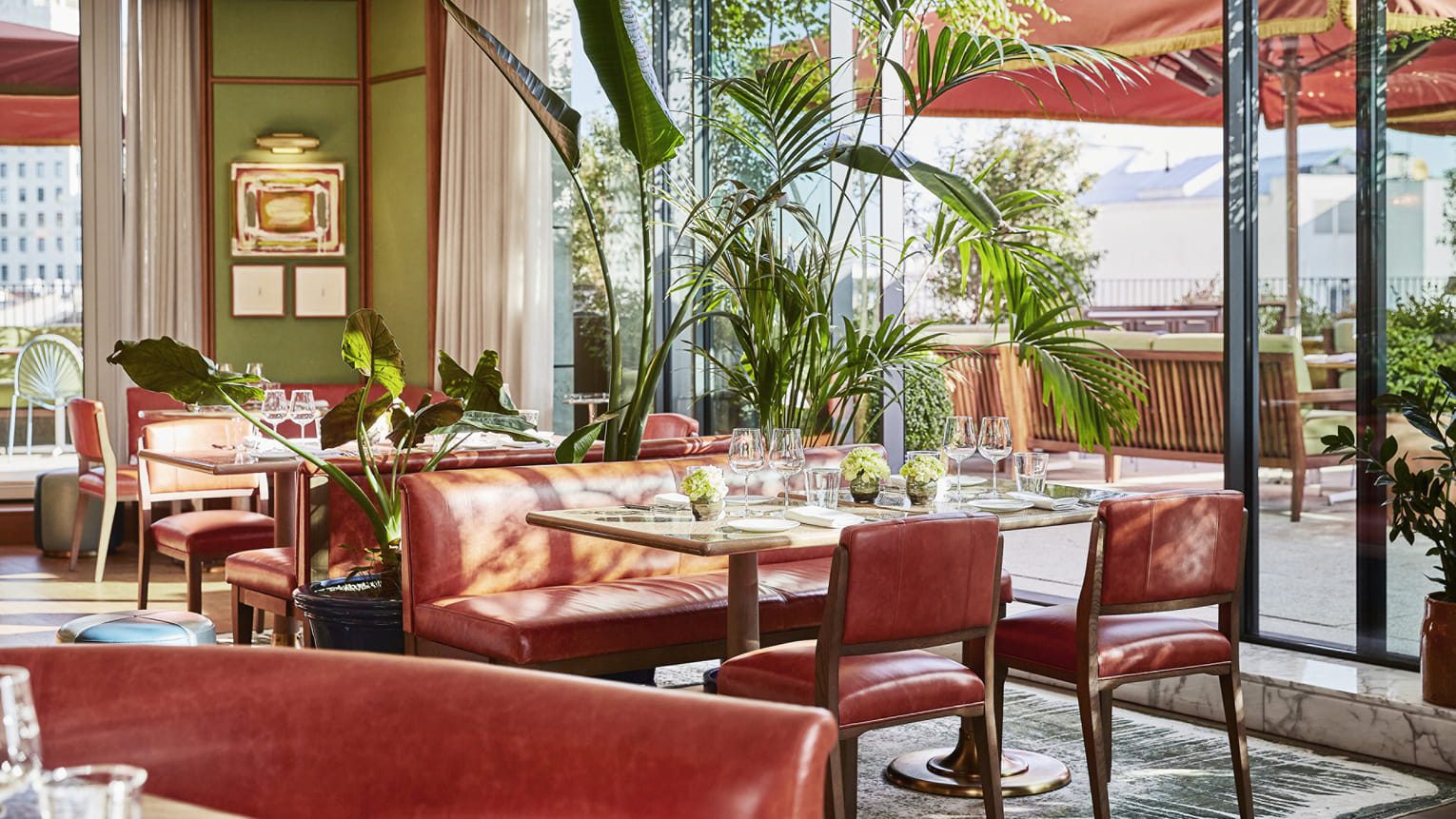 A dining area at the luxury hotel with perfectly set tables, potted plants and large windows, showcasing the views of Madrid.