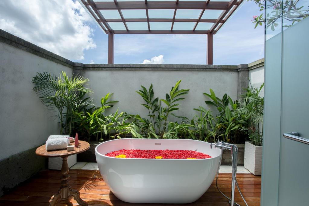 A walled terrace with plants along the back wall and a large freestanding bath in the centre, with flower petals covering the surface of the water.