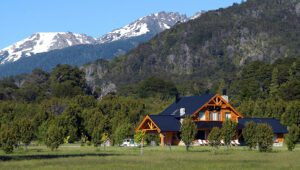 A view of part of the hotel, surrounded by large trees with a view of the mountains in the background.