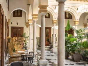 A luxury lobby with pillars and arches, a variety of potted plants, seating and tables.