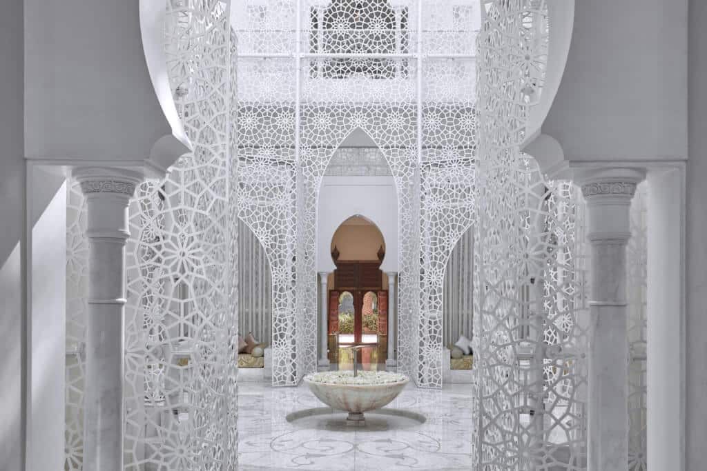 A luxury all-white entrance to the Royal Mansour Hotel with intricate detailing adorning the walls, incredible marble floors and a water feature in the centre.