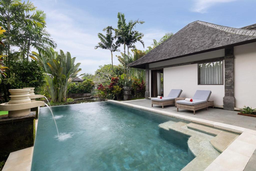 A view of the luxury accommodations at the resort from the outside, showing the outdoor pool with elegant water features, comfortable sun loungers and lush greenery in the background.