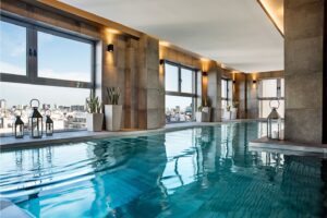 A luxury indoor pool with potted plants and candles along the pool edge, surrounded by views of Buenos Aires.