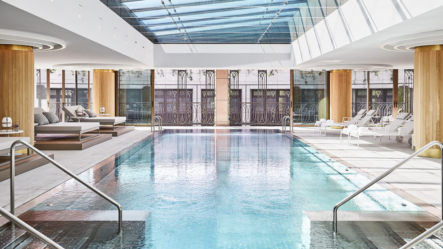 A large indoor pool at the luxury hotel, with loungers along the edge of the pool, complete with large windows and a skylight bringing in natural light.