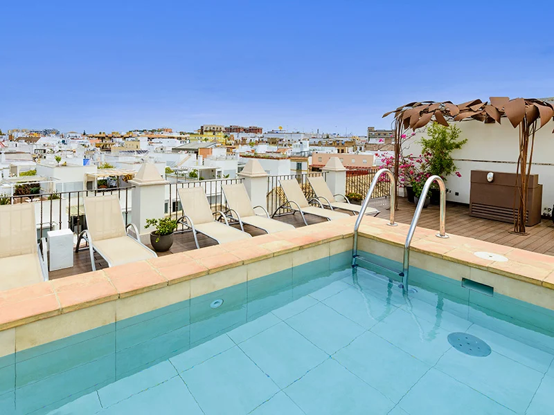 A pool on the terrace of the luxury hotel with sun loungers along the pool edge, complete with views of Seville.