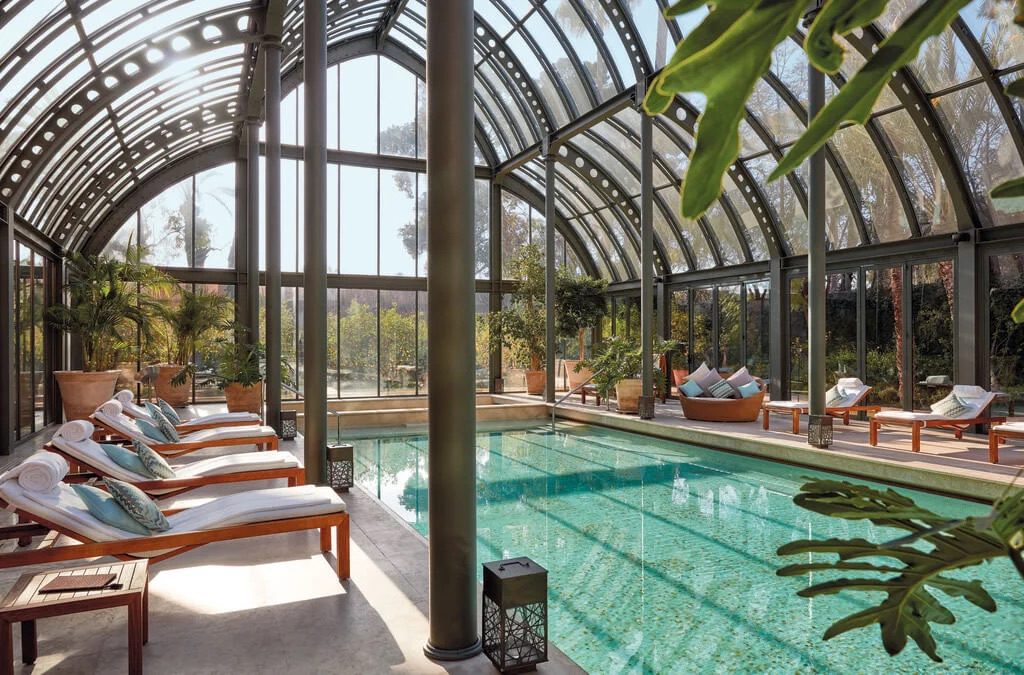 Luxury hotel pool enclosed by elegant glass walls and ceiling, offering a stunning view of the surrounding landscape, complete with relaxing lounge pool chairs.