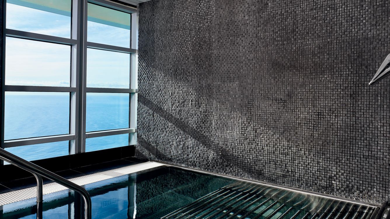 An indoor pool at the luxury spa at hotel Arts Barcelona, with a large window showcasing views of the ocean.